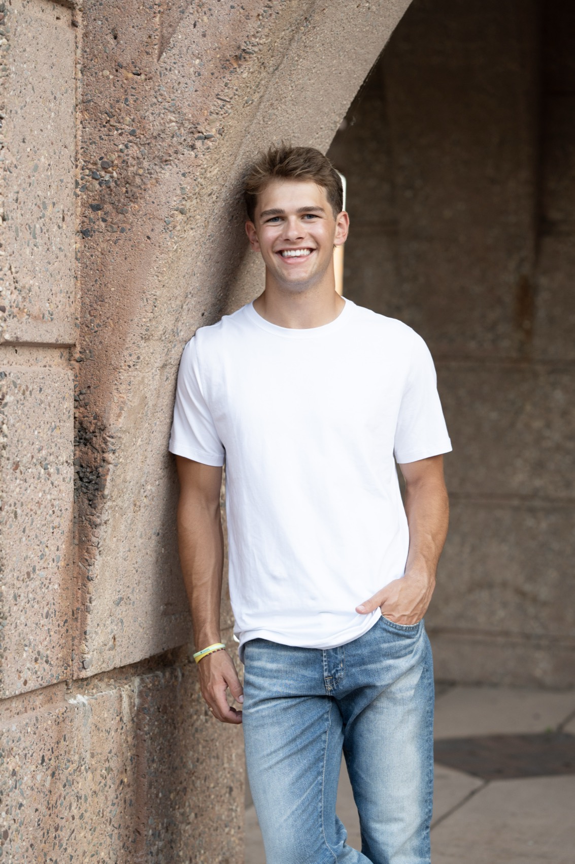 Relaxed senior in a white tee leaning against a sunlit stone arch